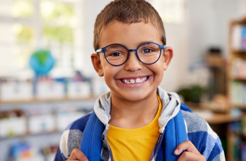 A young child at school smiling and wearing glasses.