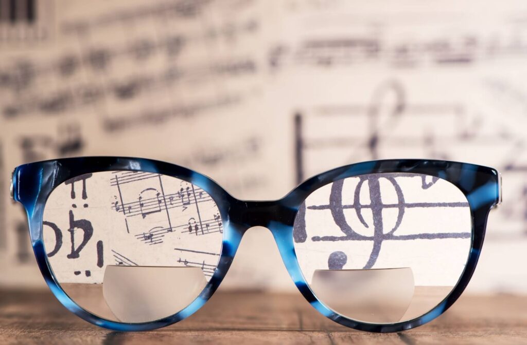 Close-up of a pair of blue tortoiseshell bifocal glasses placed in front of sheet music, with the musical notes appearing clearly through the lenses and blurred in the background.