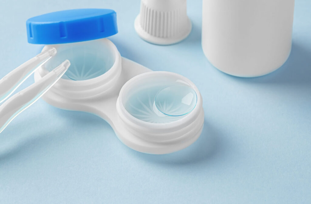 Close-up of contact lenses in a case with tweezers and a solution bottle nearby.