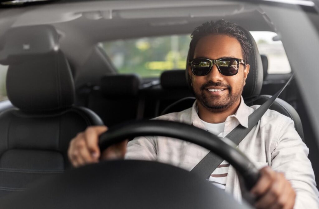 A person smiles wearing polarized sunglasses while driving in a bright, sunlit car interior.