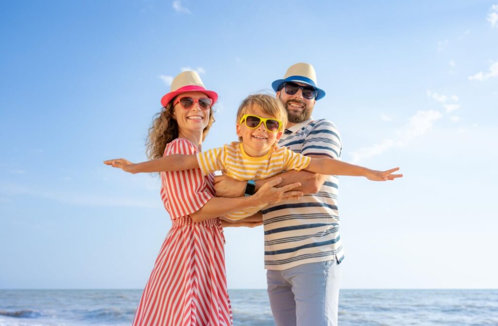 A family wearing sunglasses and summer hats, smiling at the beach on a sunny day.