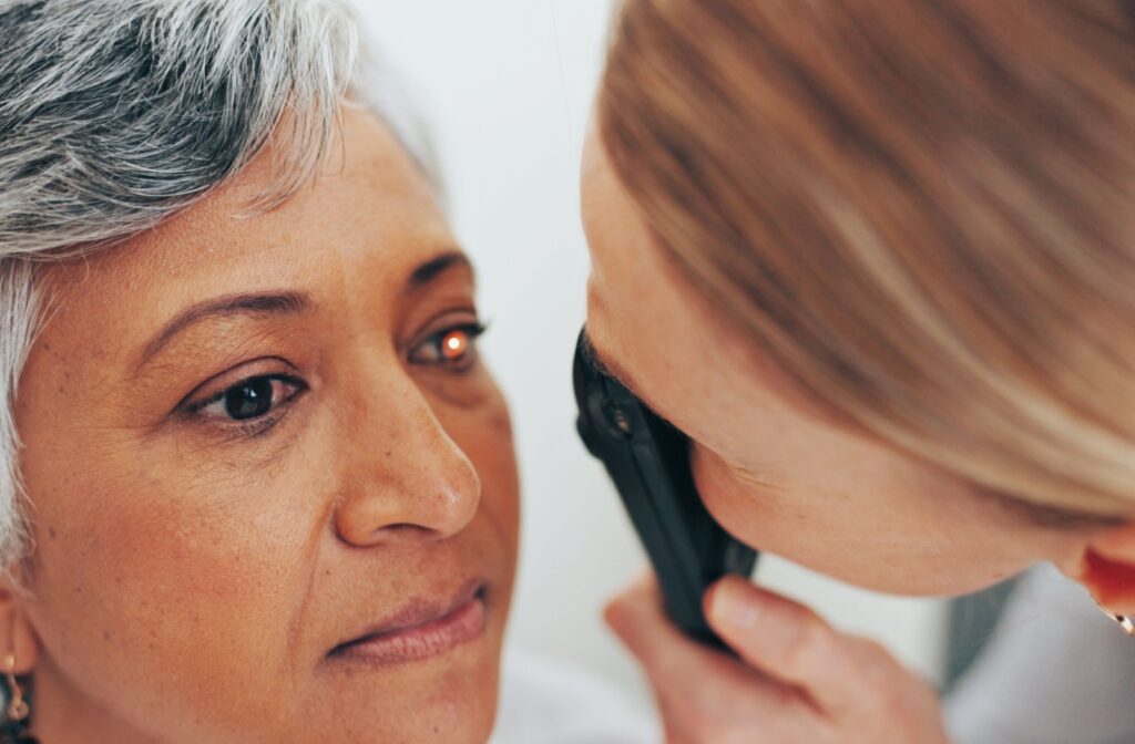 An eye doctor examines a patient's eye using an ophthalmoscope, with a small red light reflecting from her pupil during the test.