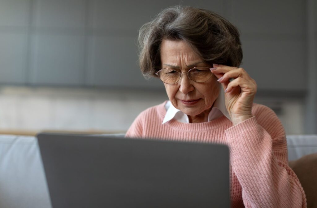 Older adult wearing glasses looking closely at a laptop screen at home.